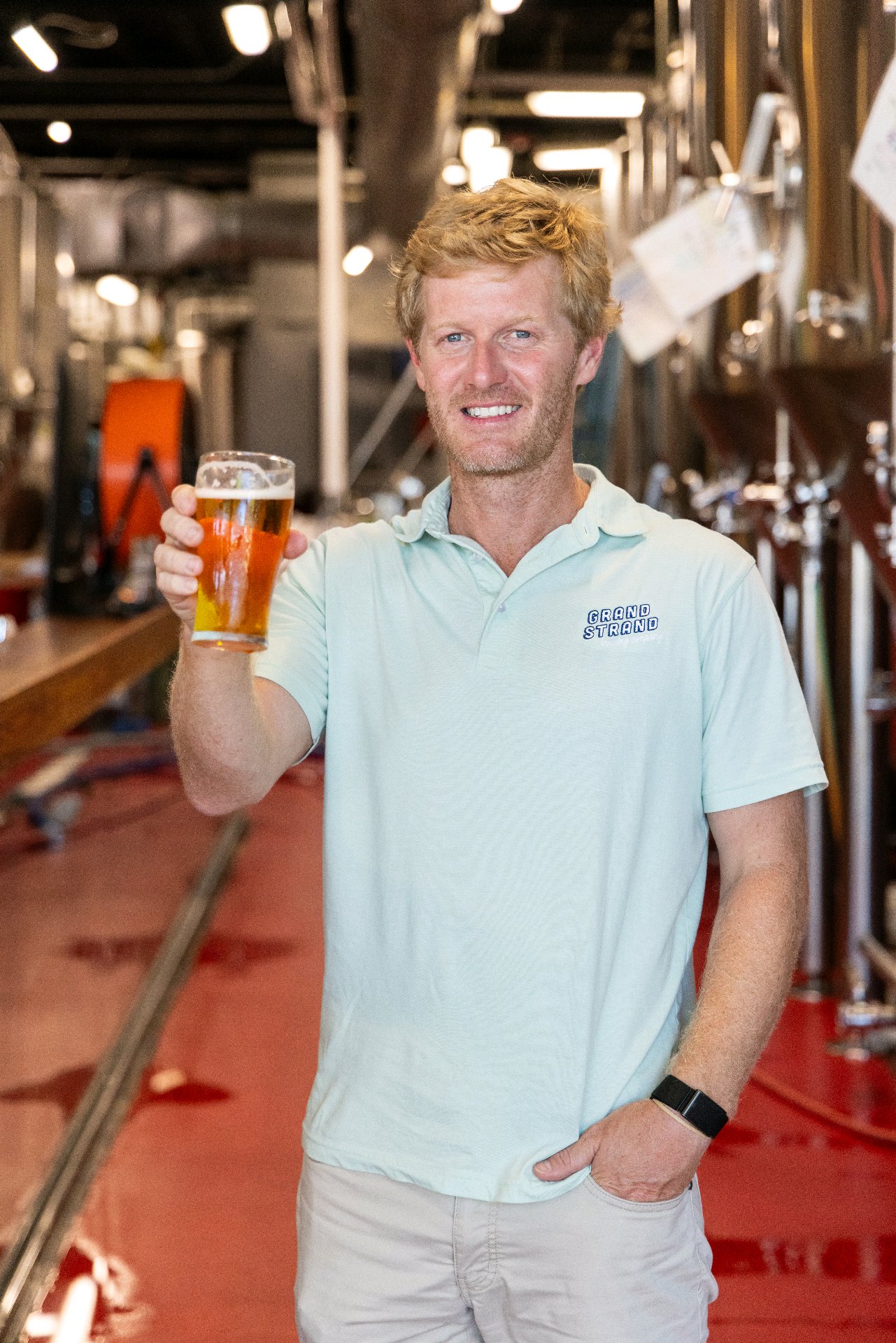 A Grand Strand Brewing Company team member raising a fresh pint inside the brewery
